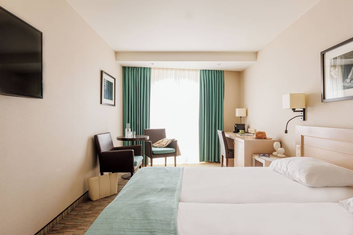 A hotel room with a bed, a desk, a chair, a TV, and a window with curtains.