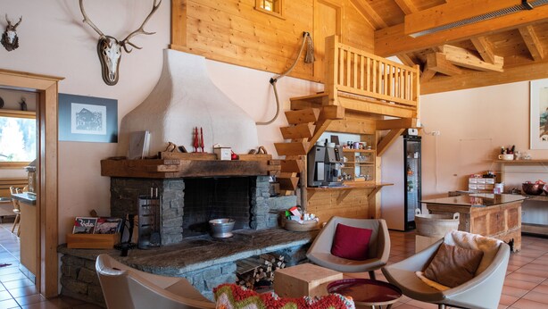 Un intérieur rustique avec une cheminée en pierre, des meubles en bois et un escalier menant à un niveau supérieur.