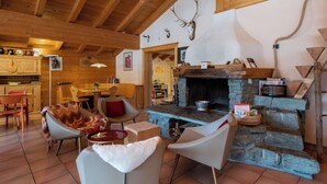 Un intérieur rustique avec une cheminée en pierre, des poutres en bois et un coin salon confortable agrémenté d’une couverture.