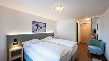 A hotel room with two beds, a nightstand, a chair, a wooden door, and a wall-mounted picture.