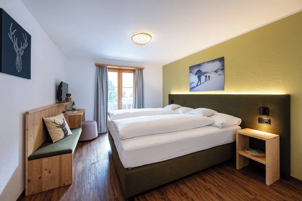 Una habitación de hotel moderna con una cama grande, un banco de madera, una mesita de noche y una lámpara de pared.