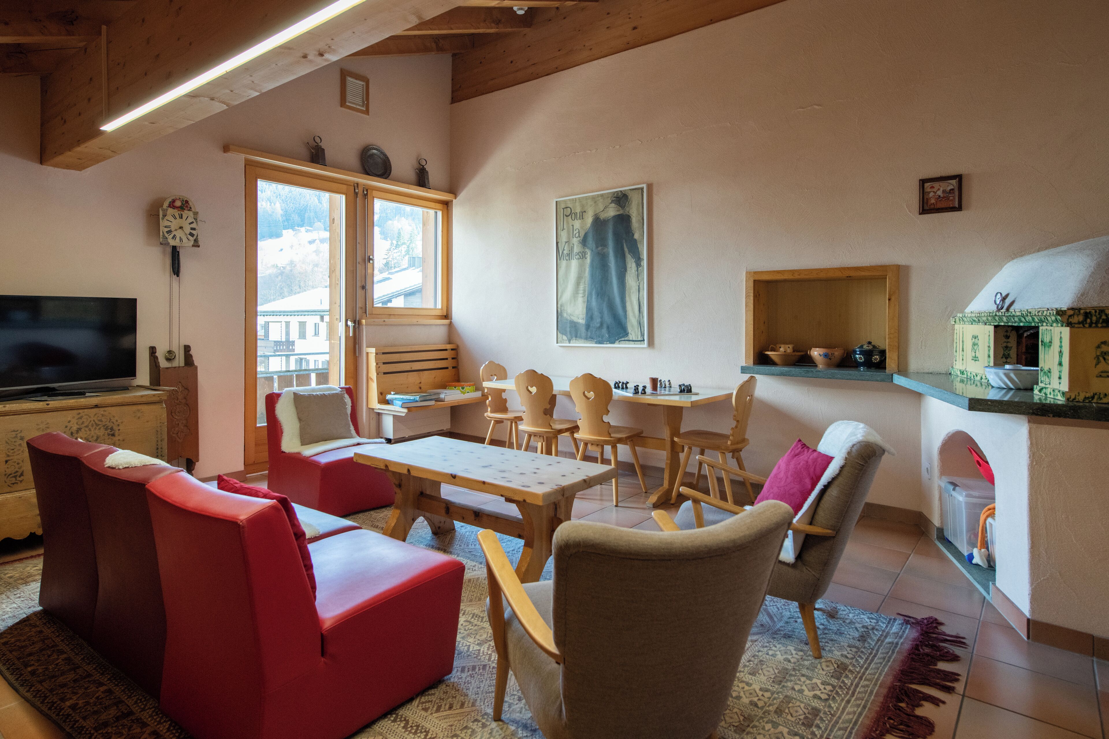 A cozy living room with a television, red sofas, a wooden table, and chairs.