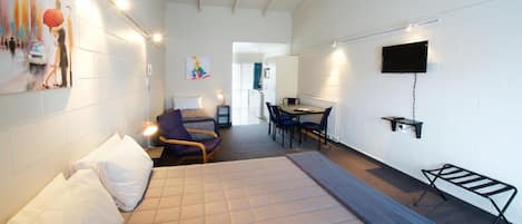 A hotel room with a bed, a desk, a chair, a TV, and a painting on the wall.