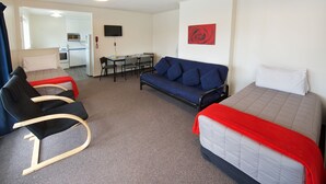 A hotel room with a bed, a sofa, a chair, a small table, and a kitchenette. - Ambassador Thermal Motel (Rotorua)