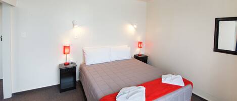 Une chambre d’hôtel avec un grand lit, deux tables de chevet avec des lampes, un téléviseur à écran plat et un miroir au mur.