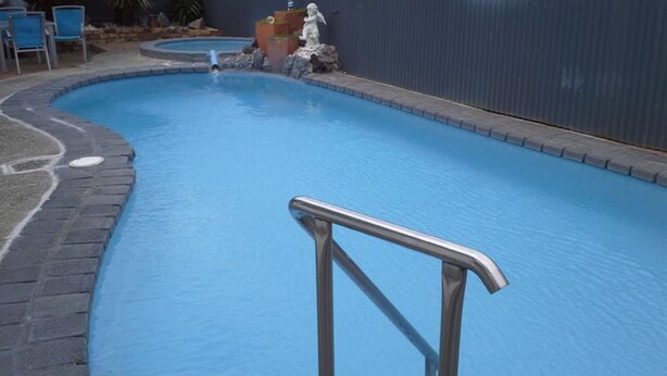A swimming pool with a metal handrail in the foreground. - Ambassador Thermal Motel (Rotorua)