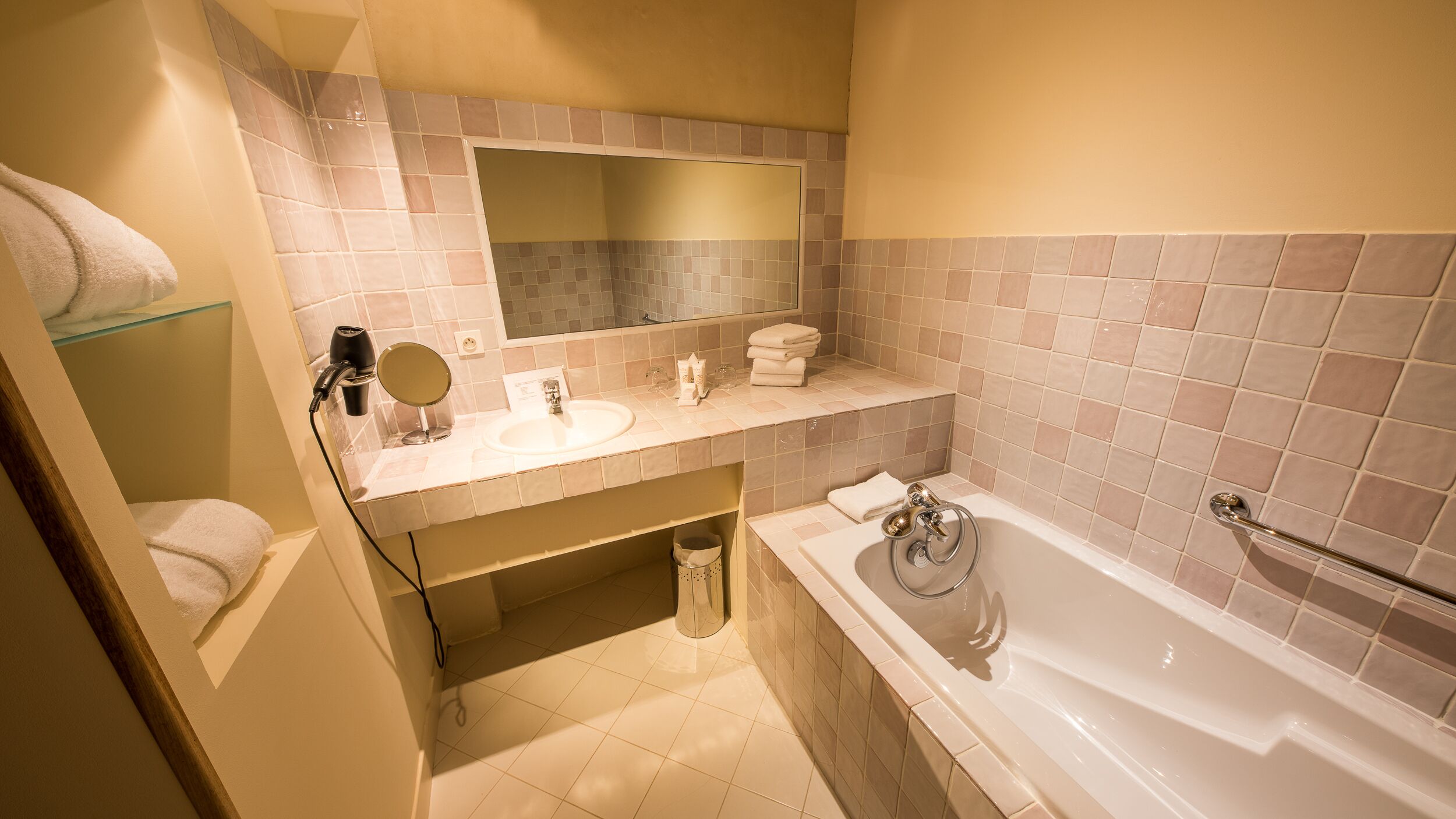 Un baño con bañera, lavamanos, espejo y toallero.