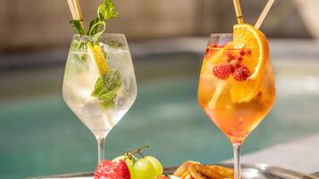 Two cocktails on a tray with strawberries and a bowl of fruit, near a pool.