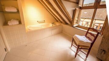 Een badkamer met een bad, een houten stoel en een raam met uitzicht op gebouwen.
