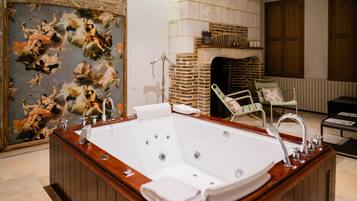 A large, freestanding bathtub in a room with a tiled floor, a fireplace, and a mural on the wall.