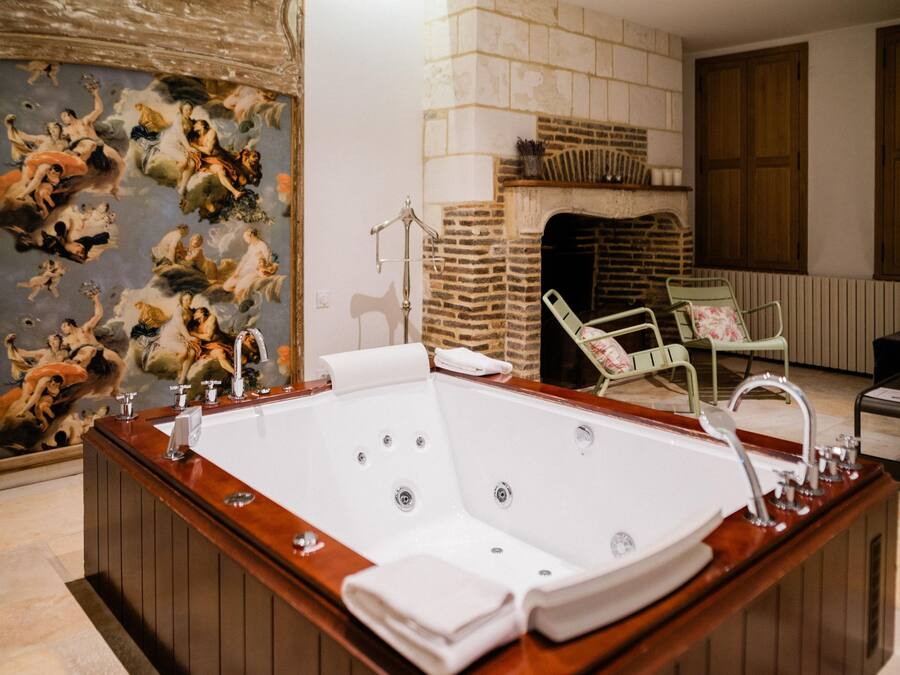A large, freestanding bathtub in a room with a tiled floor, a fireplace, and a mural on the wall.