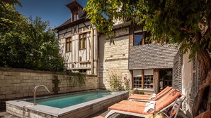 A pool area with lounge chairs, a stone wall, and a building with a tiled roof.