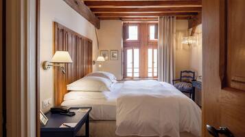 A hotel room with a wooden ceiling, a bed with white linens, a bedside table with a lamp, and a chair.