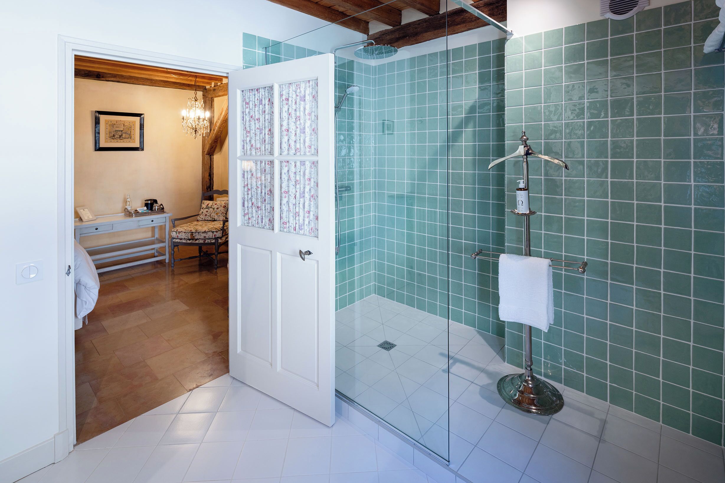 Une salle de bain avec une douche à parois de verre, un porte-serviettes et une porte donnant sur une chambre.