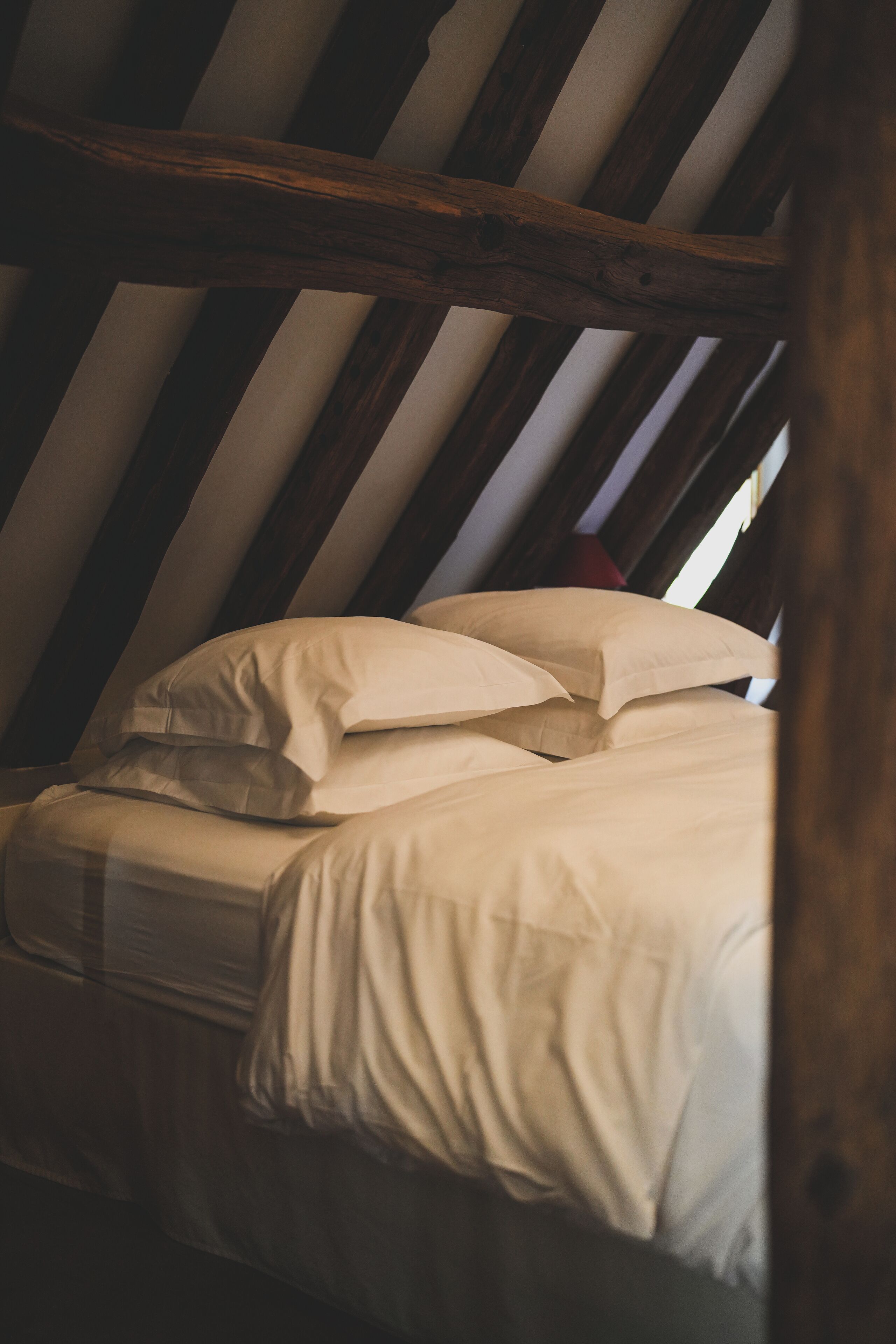 A bed with white bedding in a room with slanted wooden beams.