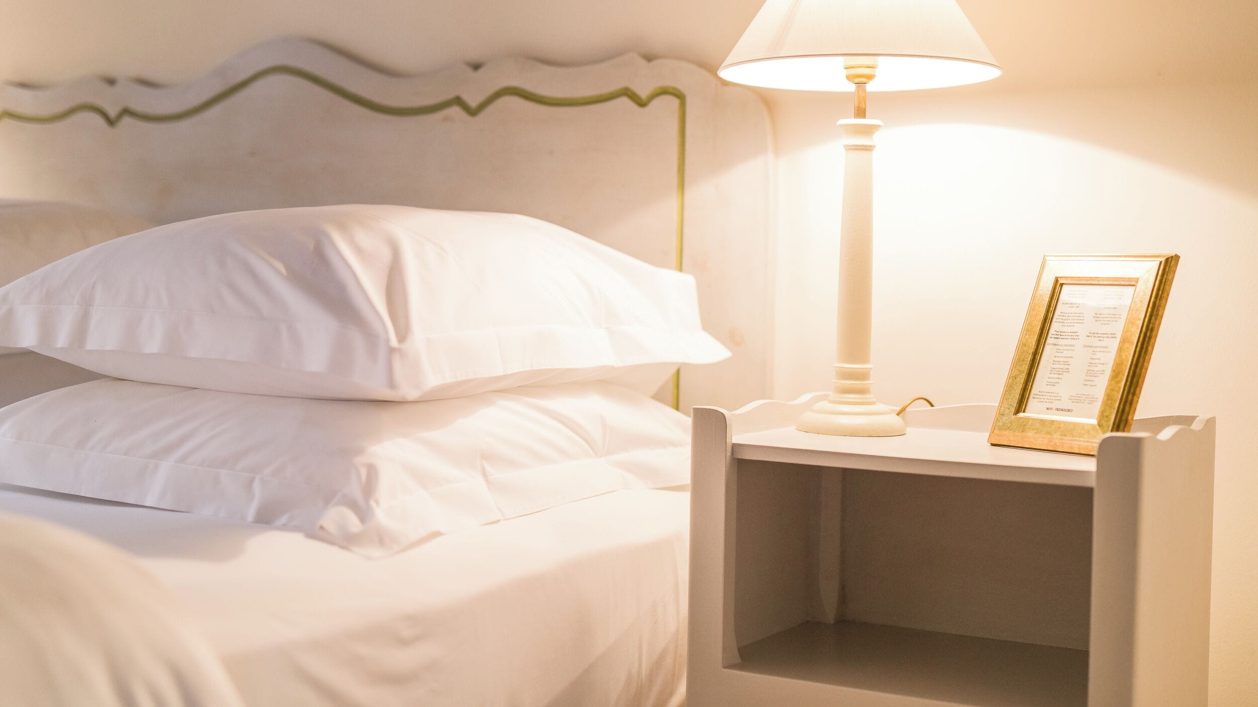A neatly made bed with white linens, a bedside lamp, and a framed menu on the nightstand.