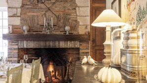 A cozy dining area with a brick fireplace, wooden chairs, a table set for a meal, and decorative items like a bird sculpture and a lamp.