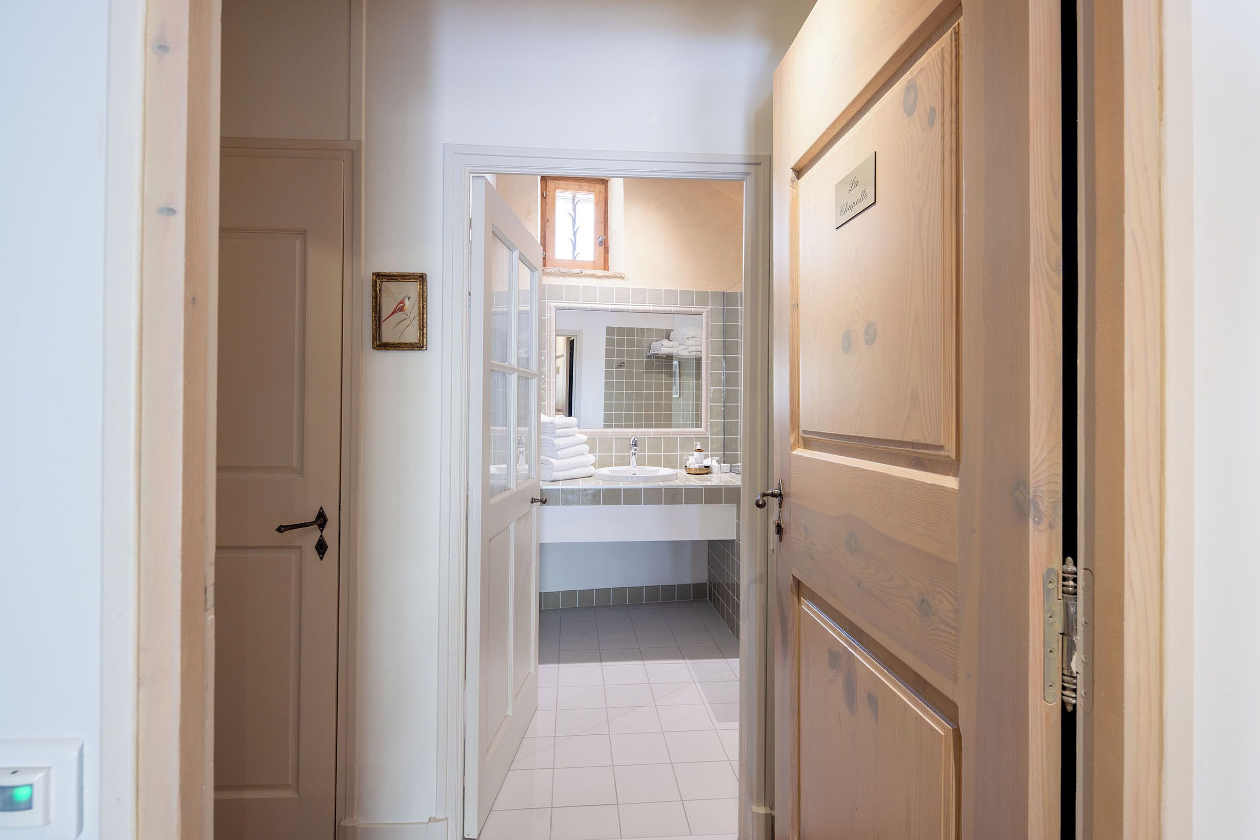 A hallway leading to a bathroom with a tiled floor, a sink, and a mirror.