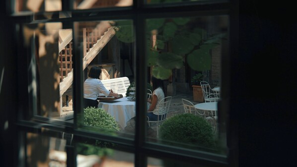 A view through a window of a dining area with a table set for two, a staircase, and a brick wall. - Le Champ des Oiseaux Hôtel & Spa 4* (Troyes)