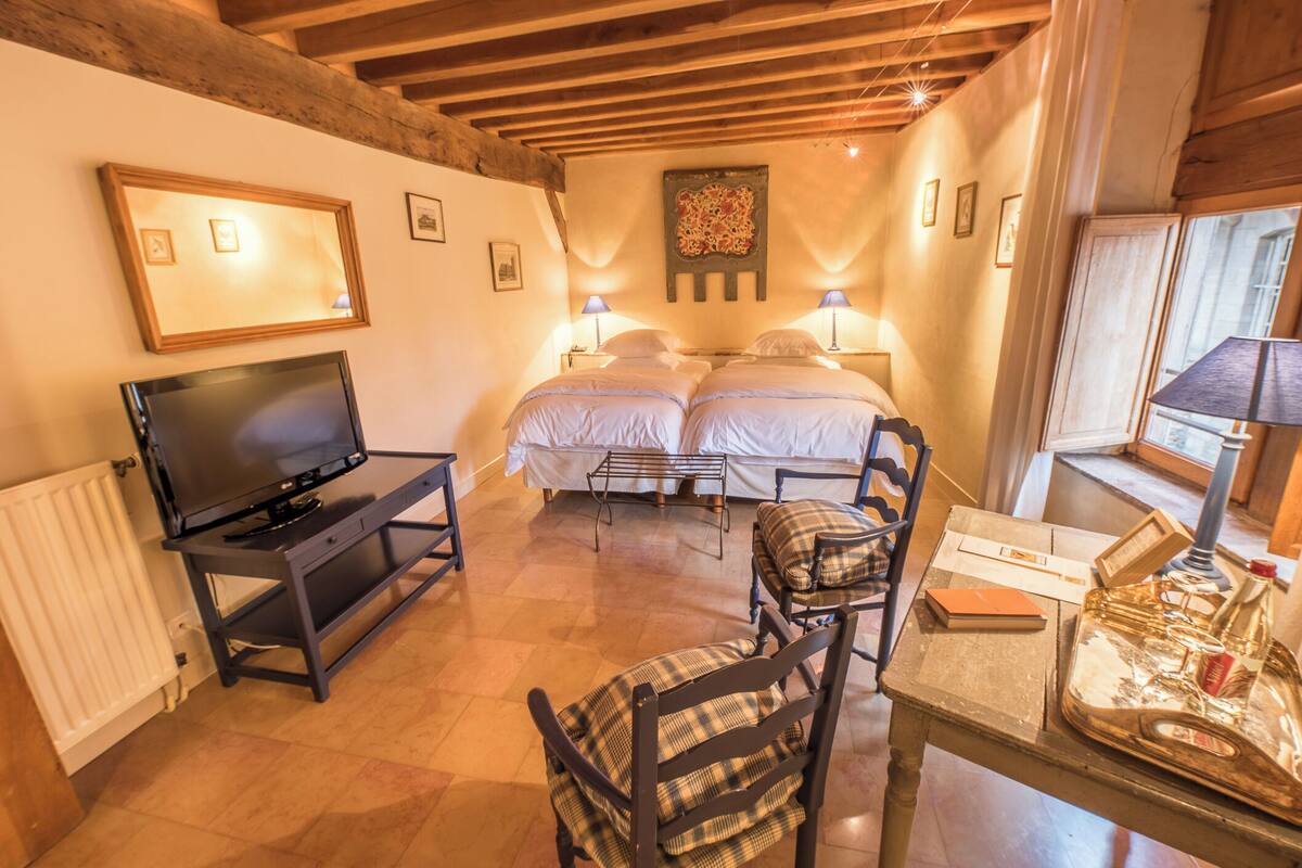 A cozy room with a bed, a TV, a table with a lamp, and a chair.