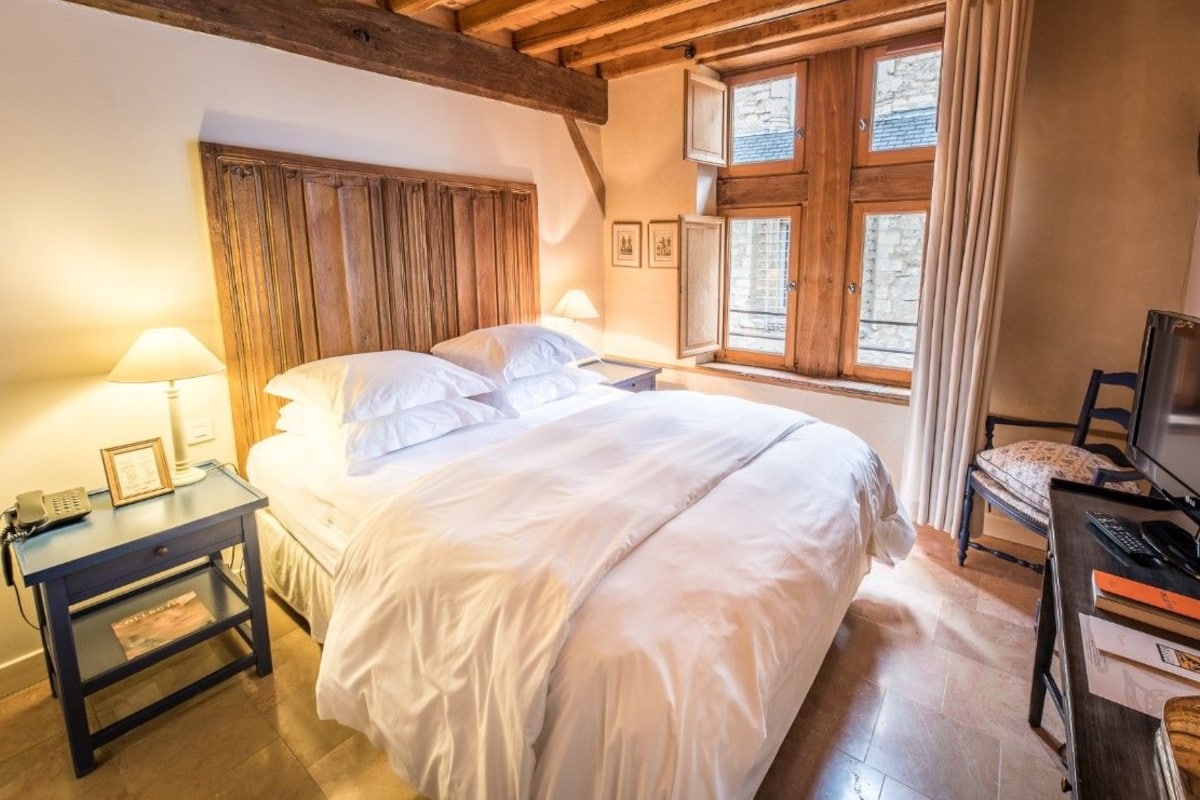 A bedroom with a bed, bedside tables, a television, and a window with curtains.