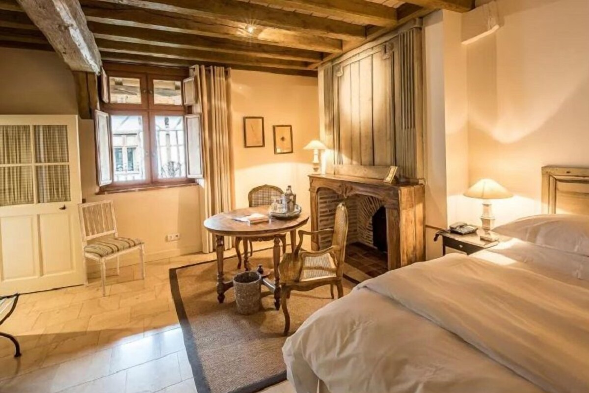 A cozy room with a fireplace, a bed, a table with chairs, and a window with curtains.