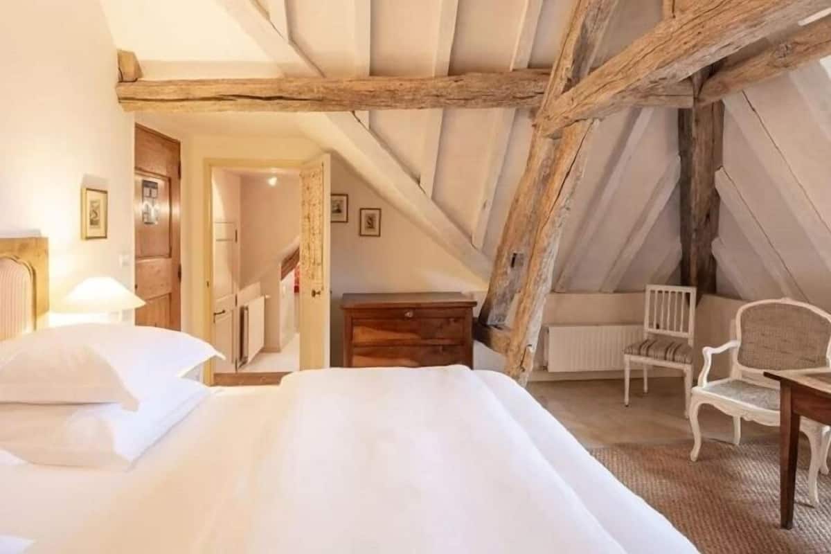 A bedroom with a sloped ceiling, a bed, a dresser, a chair, and a radiator.