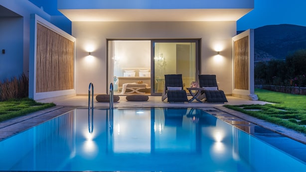 A modern outdoor pool area with a glass door leading to a bedroom, two lounge chairs, and a small table. - SunVillage Boutique Hotel (Hersonissos)
