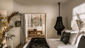 A bedroom with a bed, bedside table, mirror, hanging light fixture, and a potted plant. - SunVillage Boutique Hotel (Hersonissos)