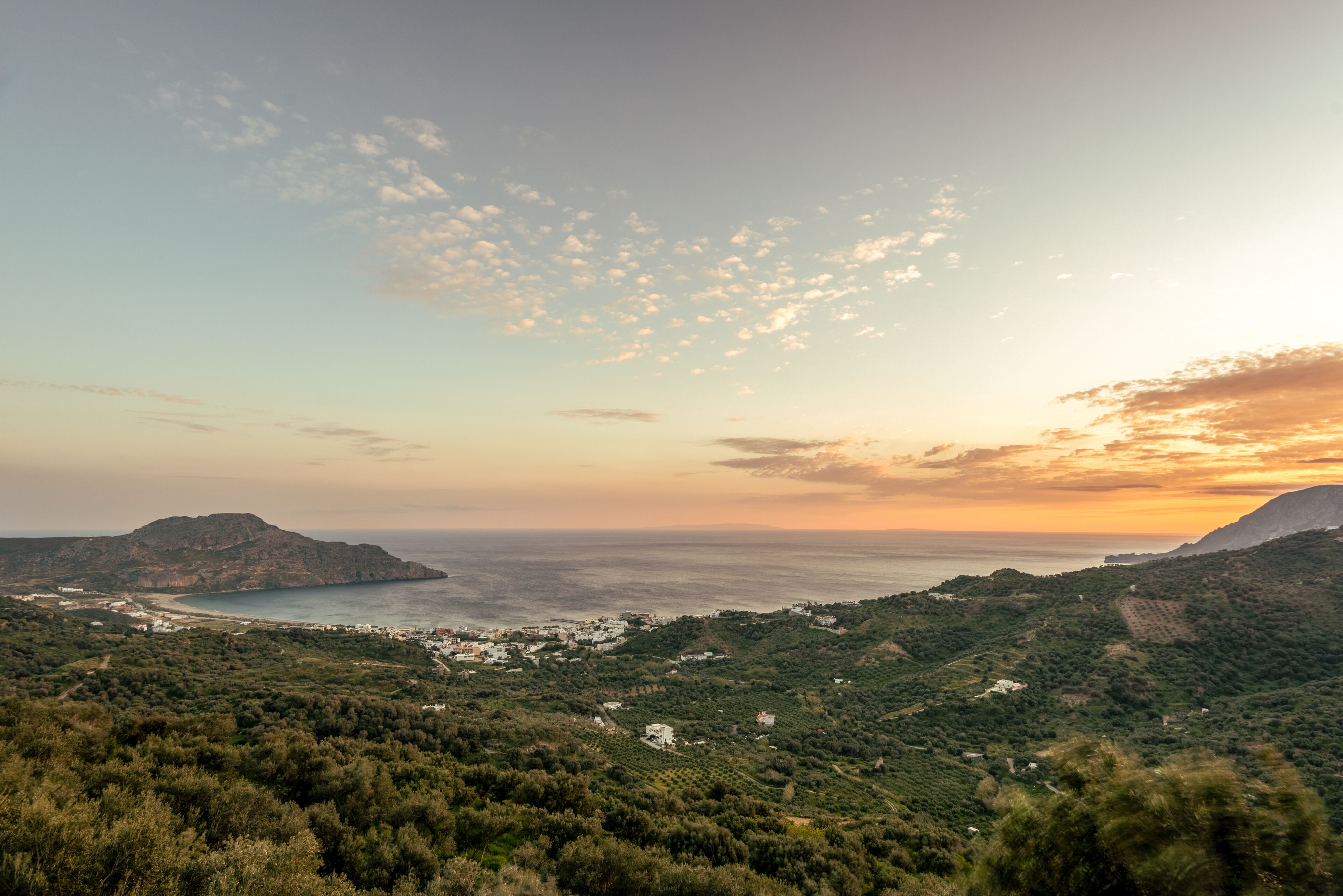 Eine Küstenlandschaft mit Blick auf das Meer, Hügel und vereinzelte Gebäude.