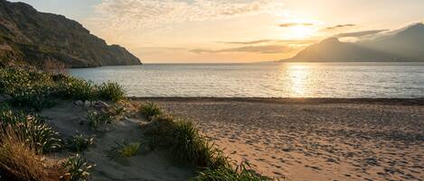 A beach with a clear view of the sea and distant mountains during sunset.