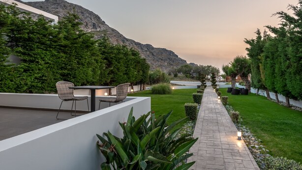 A modern outdoor patio with a seating area, a pathway, and a view of a mountain. - Plakias Suites (Agios Vasileios)