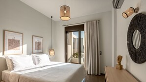 A hotel room with a large bed, a wooden table, and two wall-mounted lights. - Plakias Suites (Agios Vasileios)