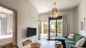 A modern hotel room with a dining area, a green sofa, and a large window offering a view of the outdoors. - Plakias Suites (Agios Vasileios)
