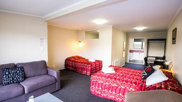 A hotel room with a sofa, two beds, a small table, and a kitchenette in the background.