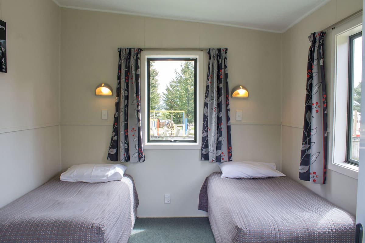 A room with two beds, a window with curtains, and wall-mounted lights.
