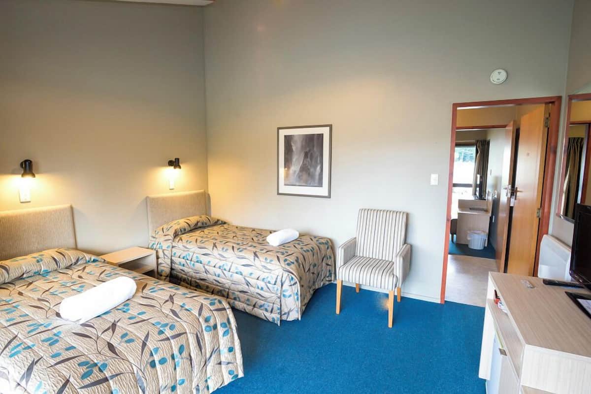 A hotel room with two beds, a chair, a desk, and a bathroom visible through an open door.