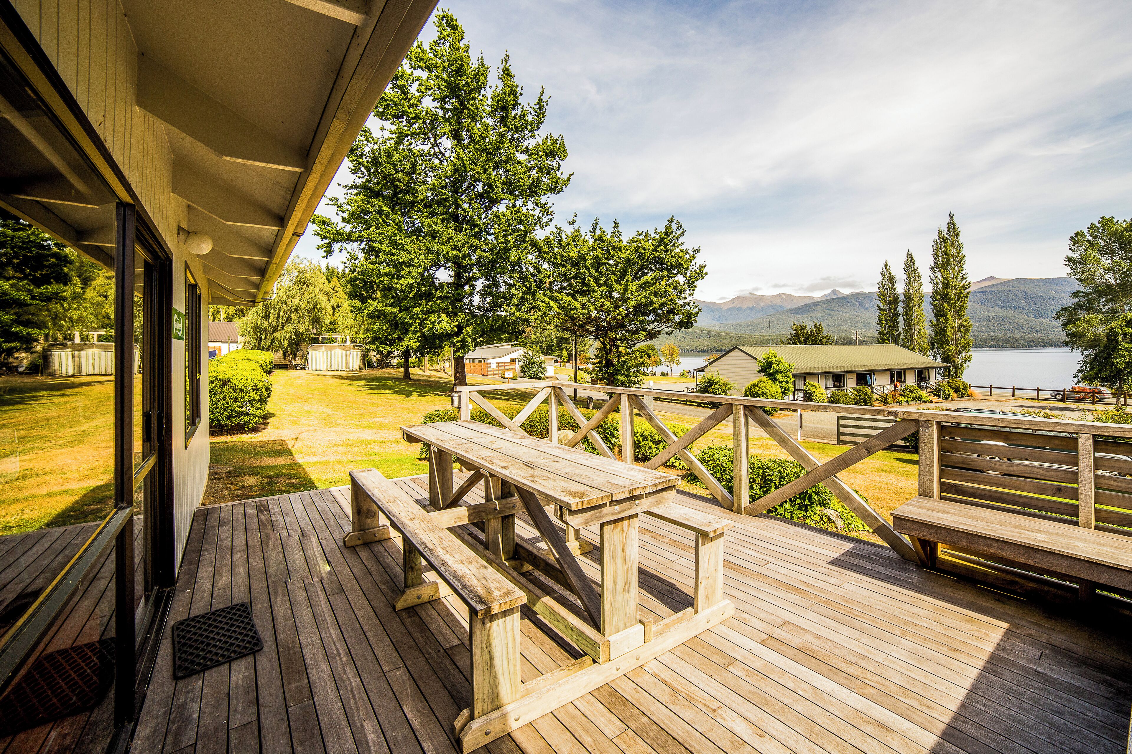 A wooden deck with picnic tables overlooking a lake and mountains.