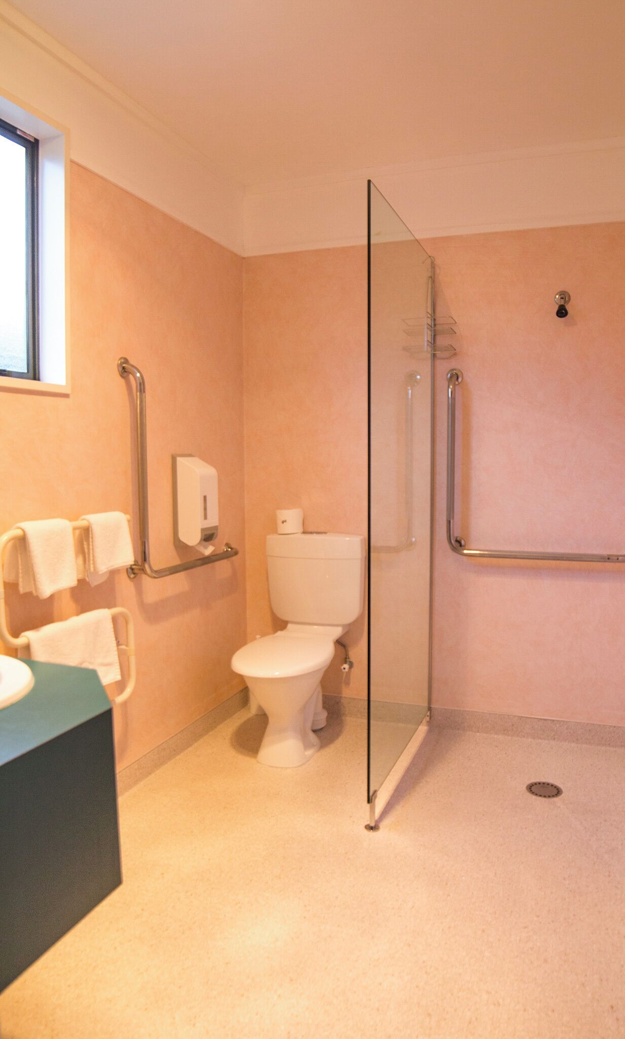 Ein Badezimmer mit Toilette, einer Duschkabine aus Glas, einem Händetrockner und einem Handtuchhalter.