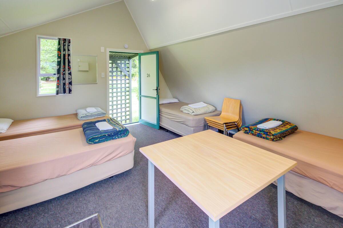 A dormitory room with two single beds, a small table, and a door leading outside.