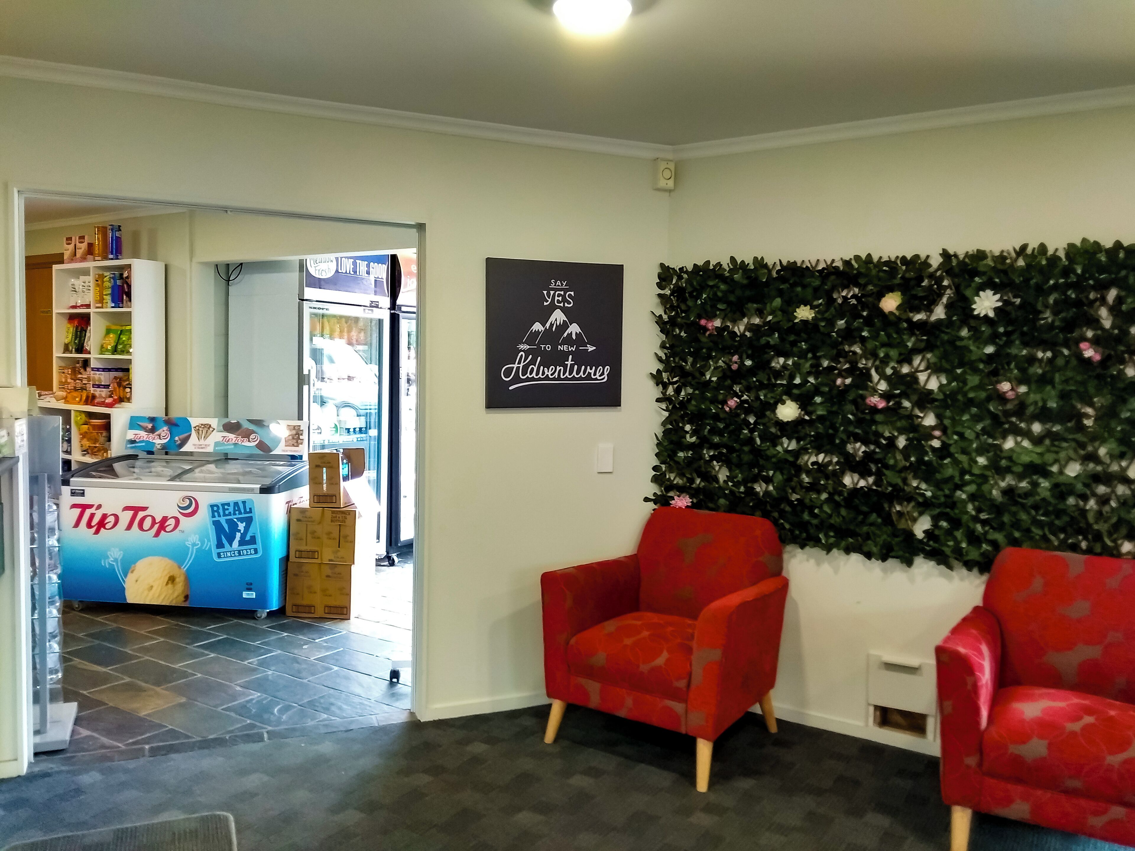 Una sala de estar con dos sillones rojos, una planta en la pared y un cartel que dice 'Yes to New Adventures'.