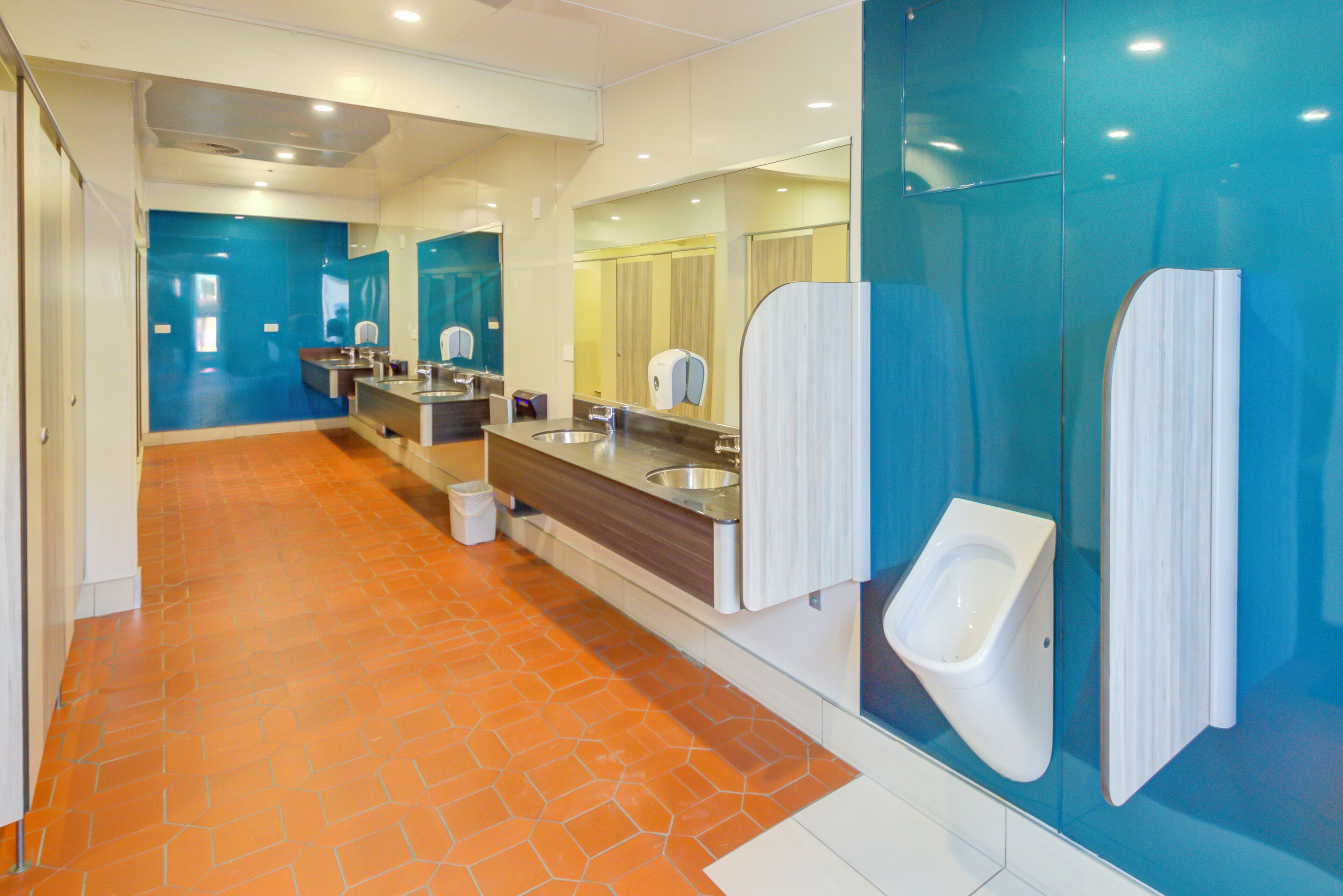 A public restroom with multiple urinals, sinks, and a trash bin.