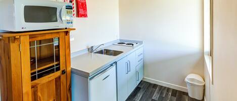 Una kitchenette compacta con microondas, lavamanos y refrigerador pequeño.