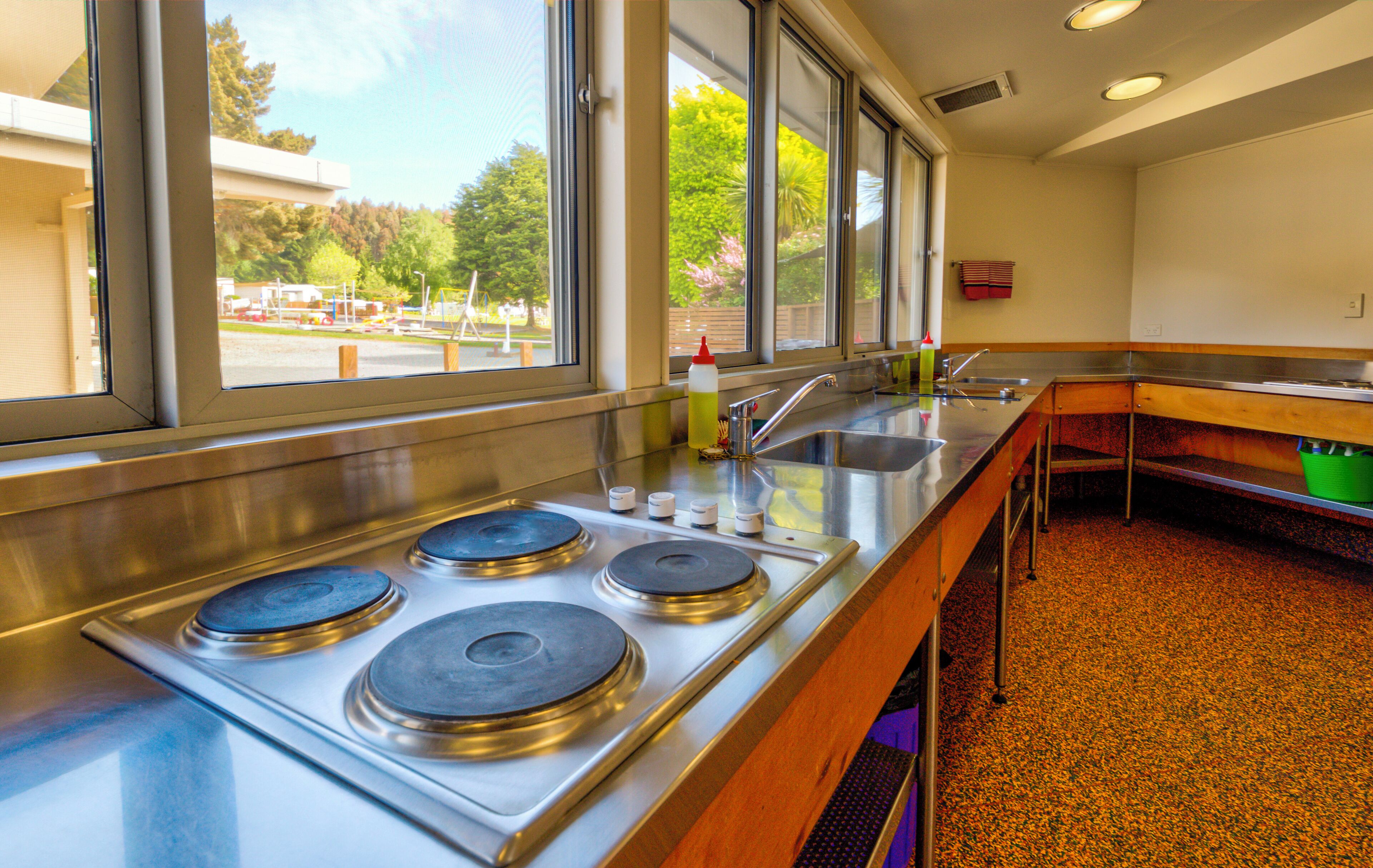 A kitchen with four burners, a sink, and a window overlooking a parking area.