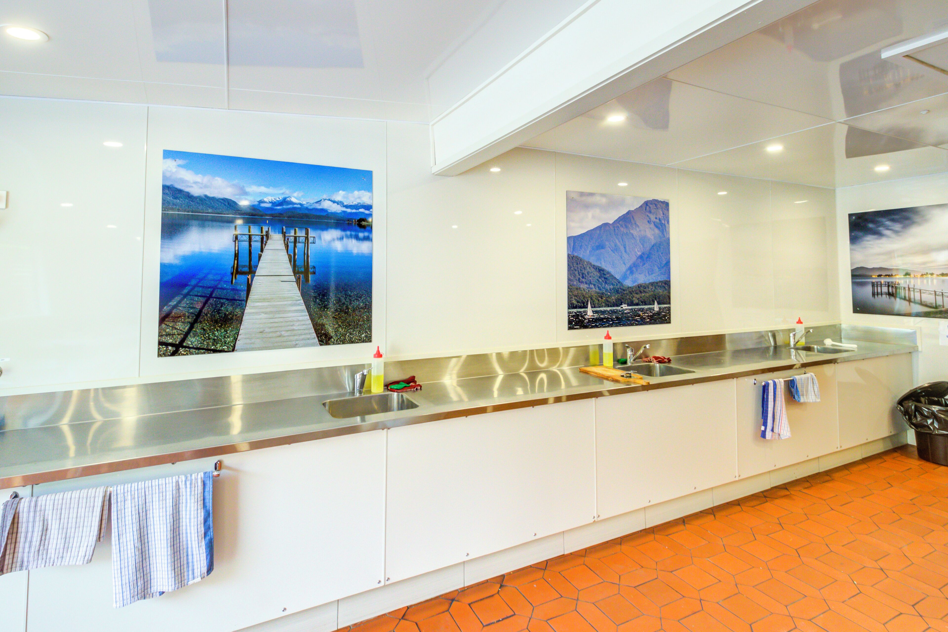A modern kitchen with a long countertop, stainless steel appliances, and three large landscape paintings on the wall.