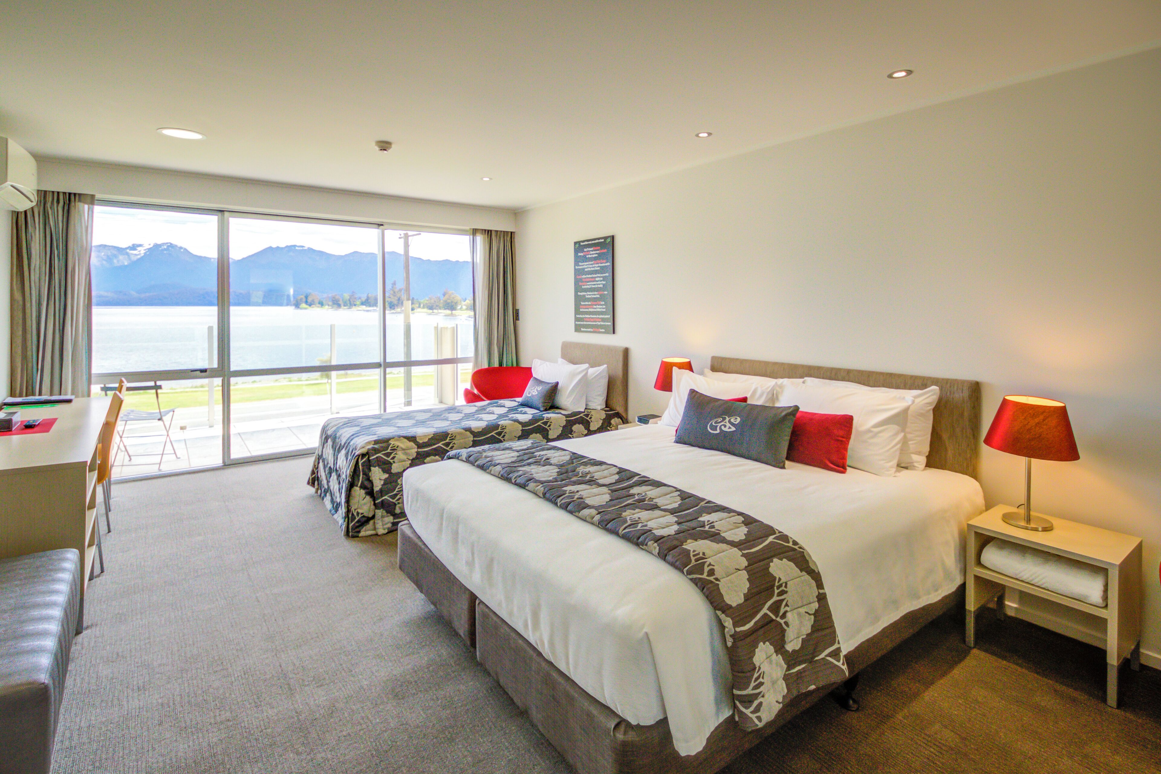 Habitación de hotel con dos camas, un escritorio y vistas al lago.