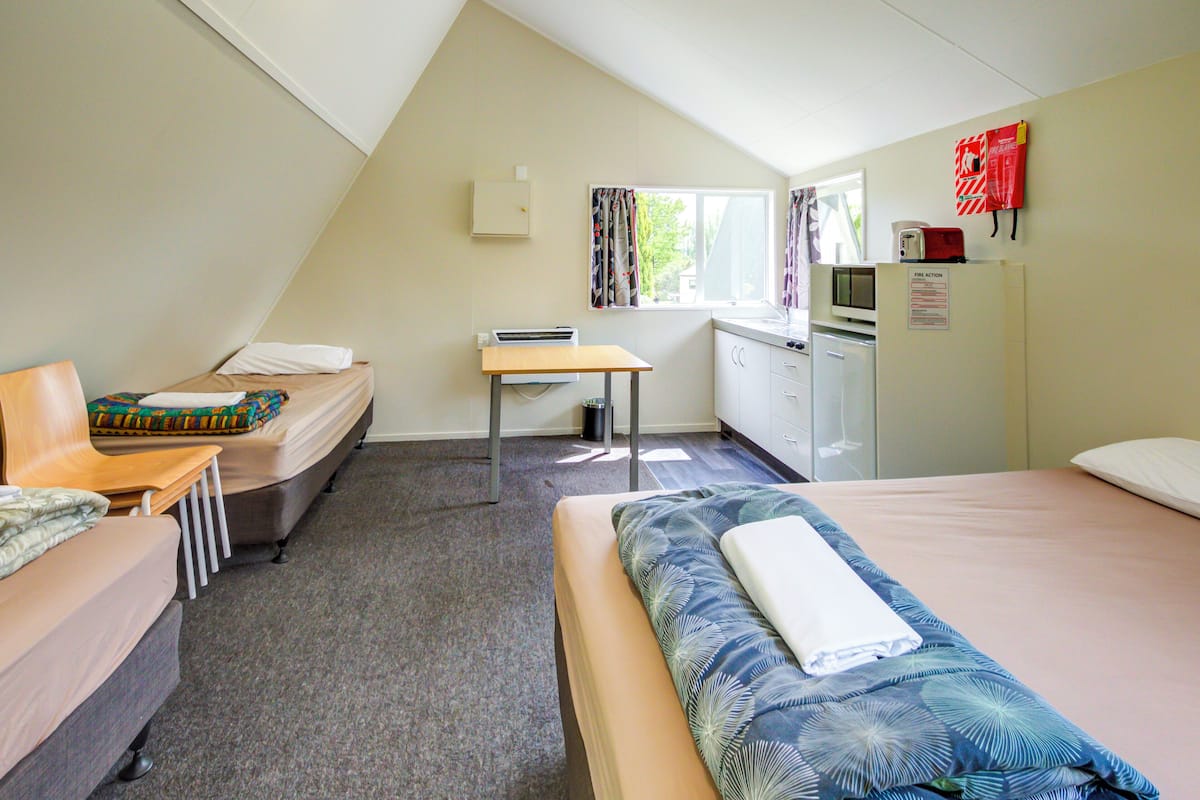 A room with a bed, a desk, a chair, a small table, a microwave, and a refrigerator.