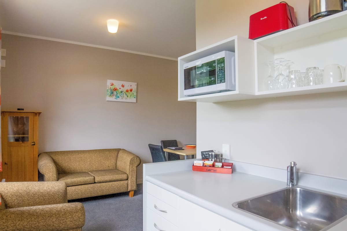 A compact living space with a kitchenette, a sofa, a dining area, and a wall-mounted shelf with kitchenware.