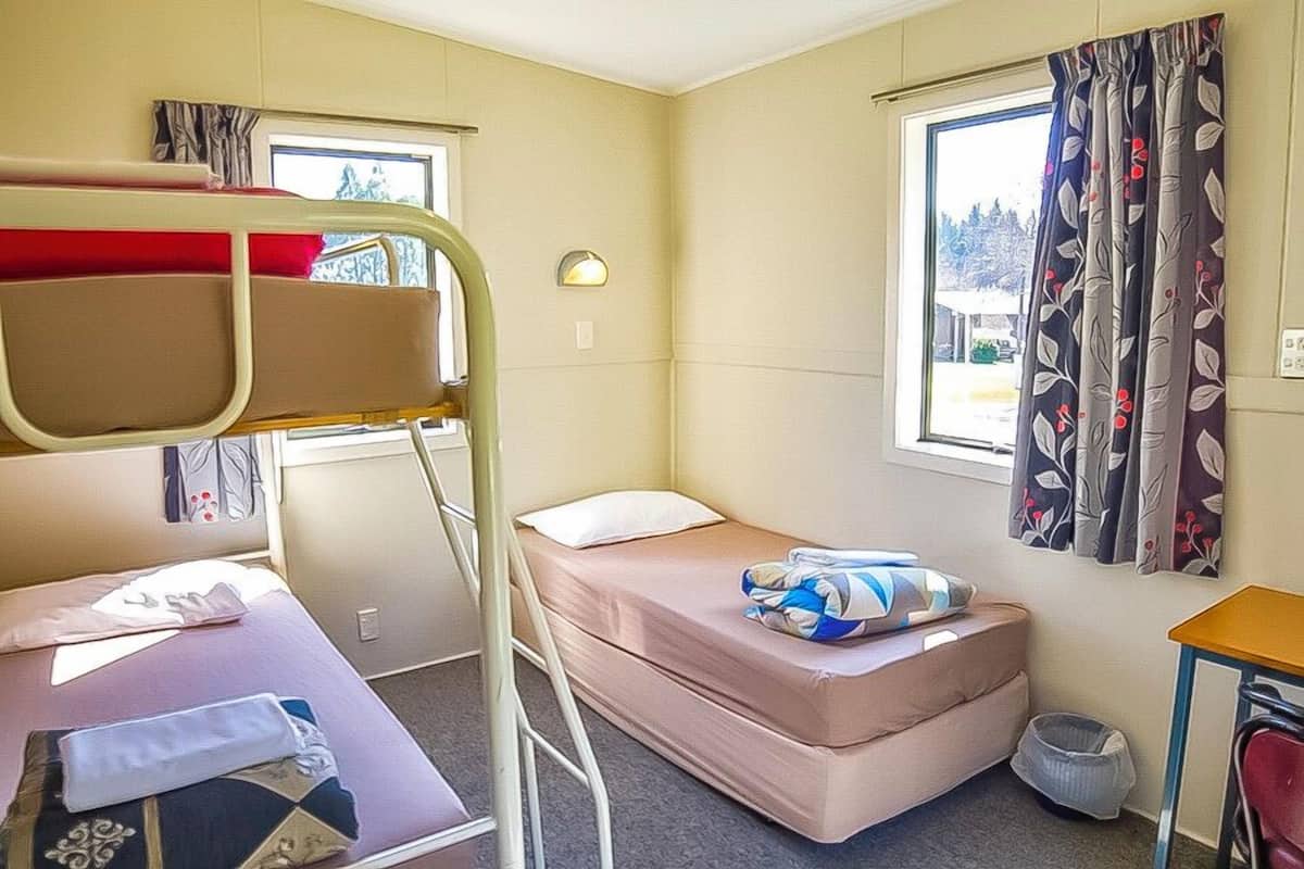 A compact room with bunk beds, a single bed, a small desk, and a window with curtains.