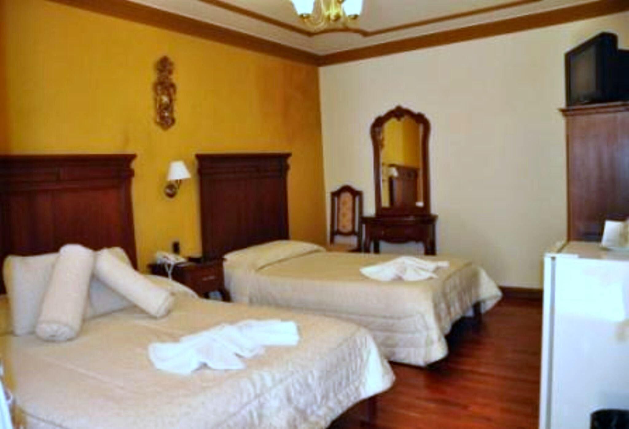 Een hotelkamer met twee bedden, een houten vloer, een spiegel en een televisie.